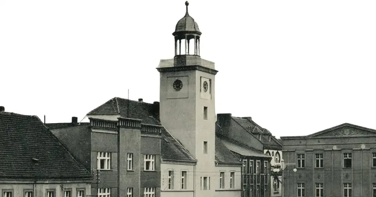 A black and white photo of a small European village with a prominent clock tower in the center.